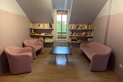 Salle de réunion lumineuse avec tables disposées en U et chaises orange, entourée de grandes fenêtres.