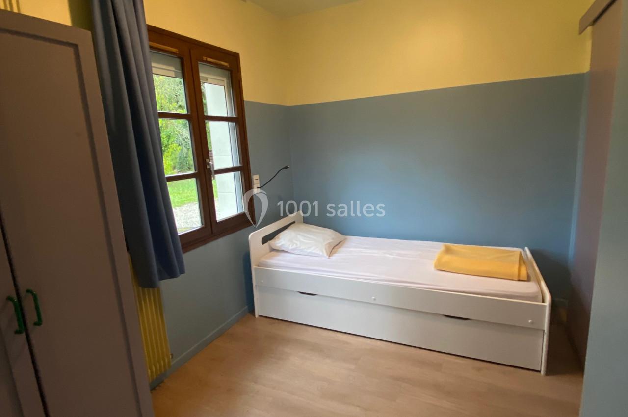 Chambre simple avec lit une place, armoire, fenêtre avec rideau bleu et murs peints en jaune et bleu.