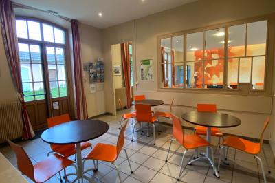 Salle de réunion lumineuse avec tables disposées en U et chaises orange, entourée de grandes fenêtres.