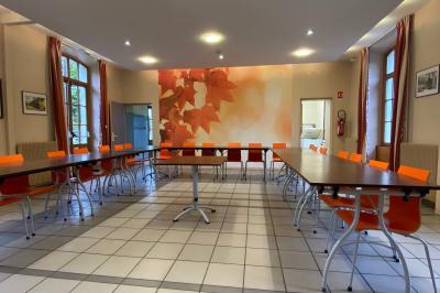 Salle de réunion lumineuse avec tables disposées en U et chaises orange, entourée de grandes fenêtres.