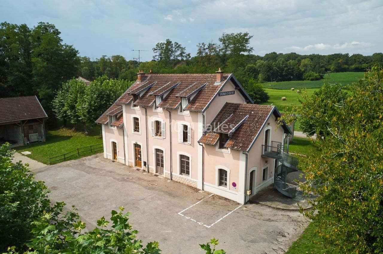 Bâtiment à deux étages avec façade rose, toit en tuiles et environnement rural verdoyant.