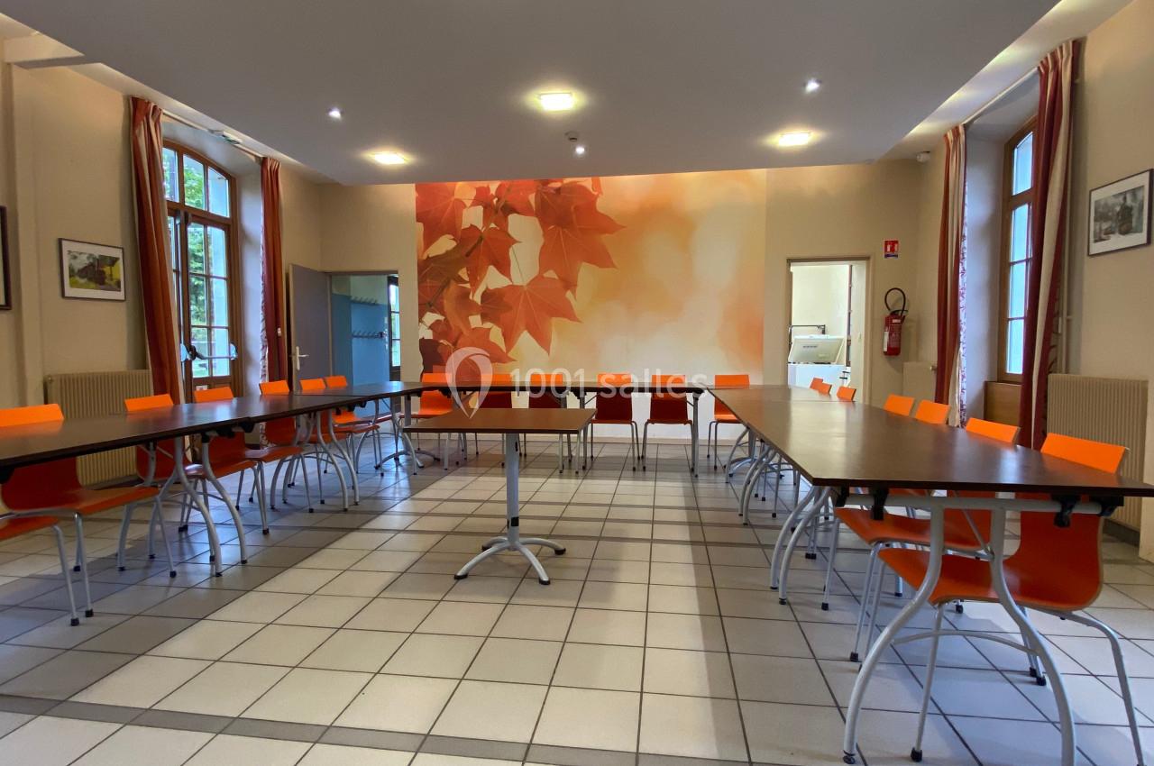 Salle de réunion lumineuse avec tables disposées en U, chaises orange et mur décoré de motifs de feuilles d'automne.