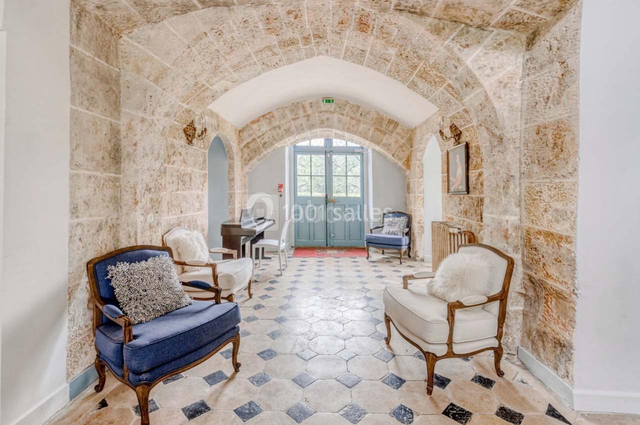 Salon lumineux avec voûtes en pierre, fauteuils élégants, piano et sol en carreaux noirs et blancs.