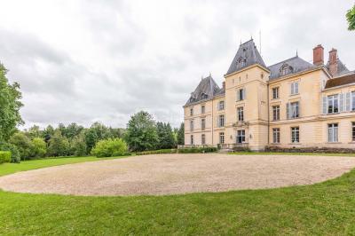 Façade d'un château avec toit en ardoise, entouré de jardins symétriques et allées gravillonnées.
