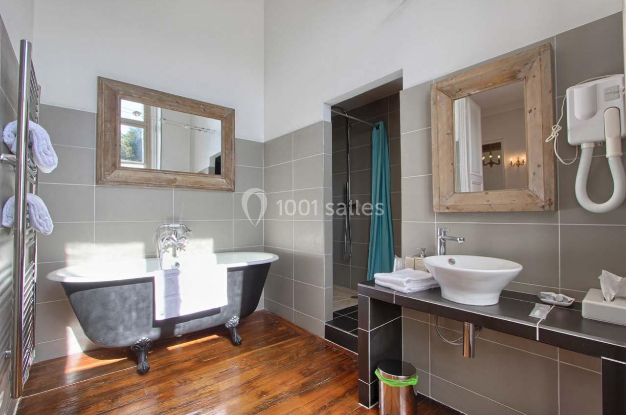 Salle de bain lumineuse avec baignoire sur pieds, lavabo moderne, miroir encadré en bois et douche ouverte.