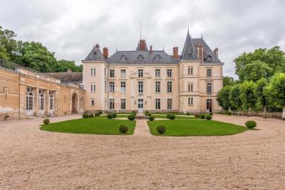 Façade d'un château avec toit en ardoise, entouré de jardins symétriques et allées gravillonnées.