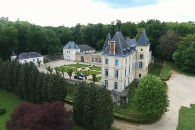 Façade d'un château avec toit en ardoise, entouré de jardins symétriques et allées gravillonnées.