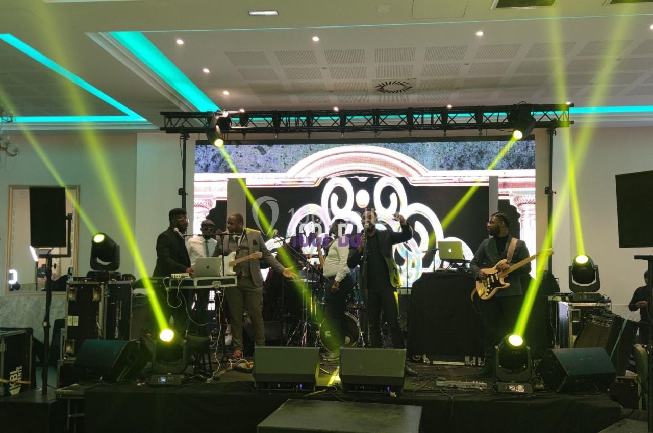 Un groupe de musiciens se produit sur scène avec des éclairages colorés et un écran décoratif en arrière-plan.