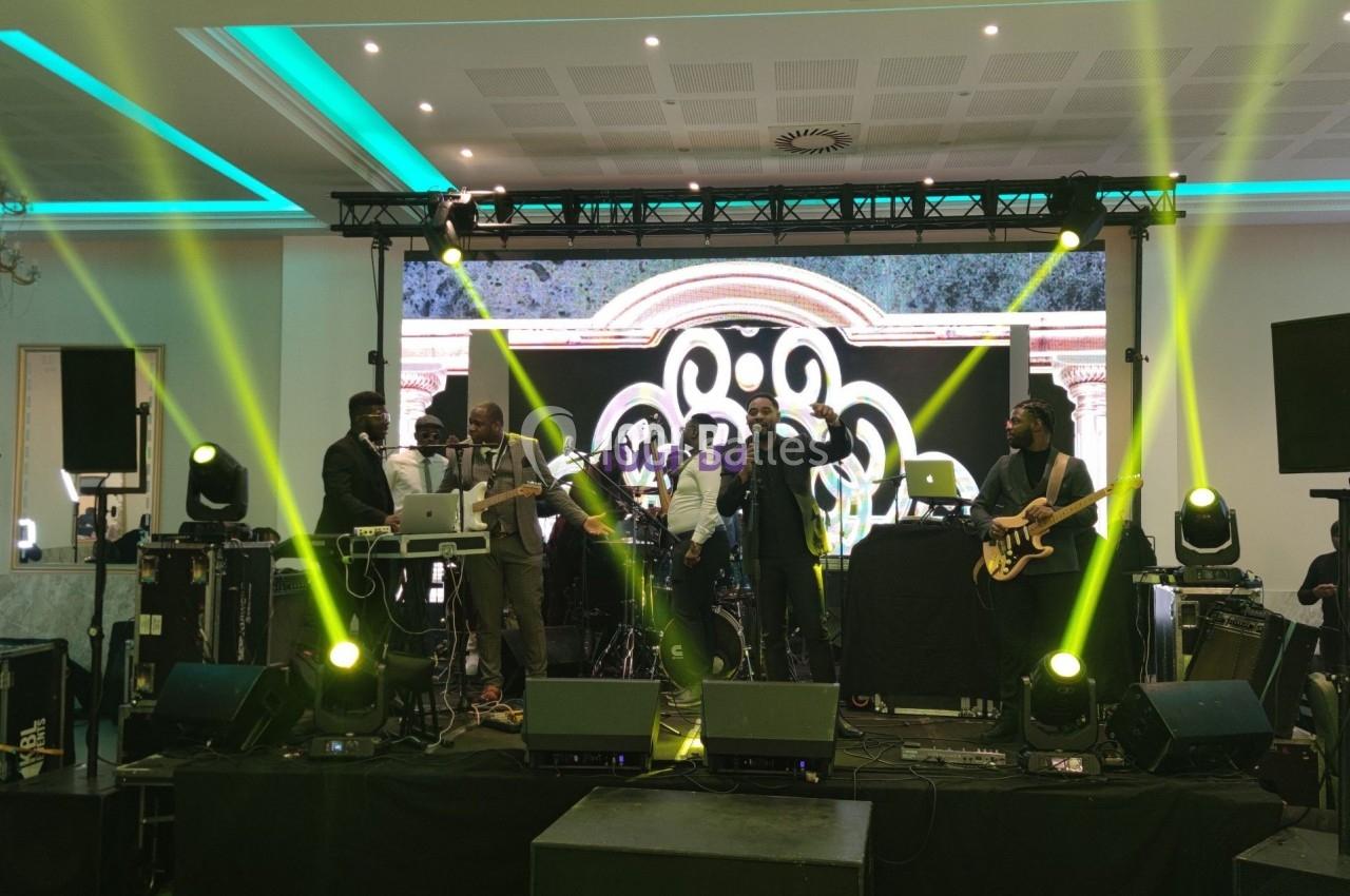 Groupe de musiciens sur scène avec éclairages colorés et écran lumineux en arrière-plan dans une salle de spectacle.