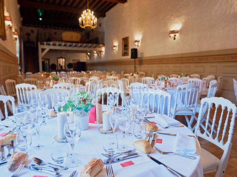 Salle de réception élégante avec tables rondes dressées, nappes blanches, chandelles et décorations florales.