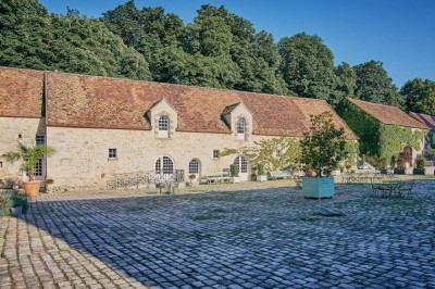 Deux portes en pierre et bois s'ouvrent sur des pièces lumineuses avec mobilier classique et parquet.