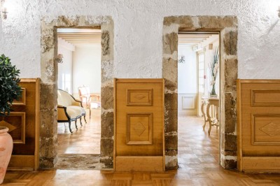 Deux portes en pierre et bois s'ouvrent sur des pièces lumineuses avec mobilier classique et parquet.
