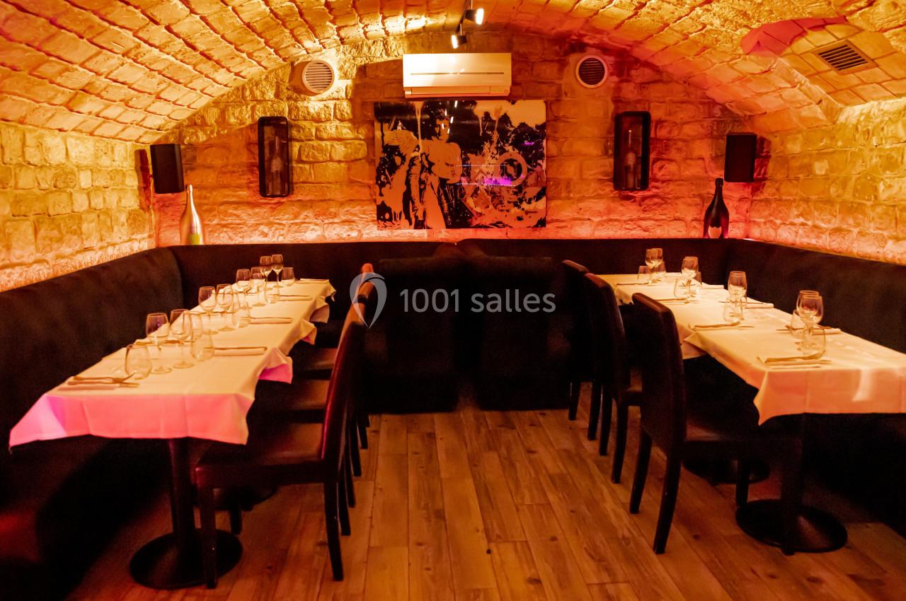 Salle de restaurant voûtée en pierre avec tables dressées, nappes blanches et éclairage chaleureux.