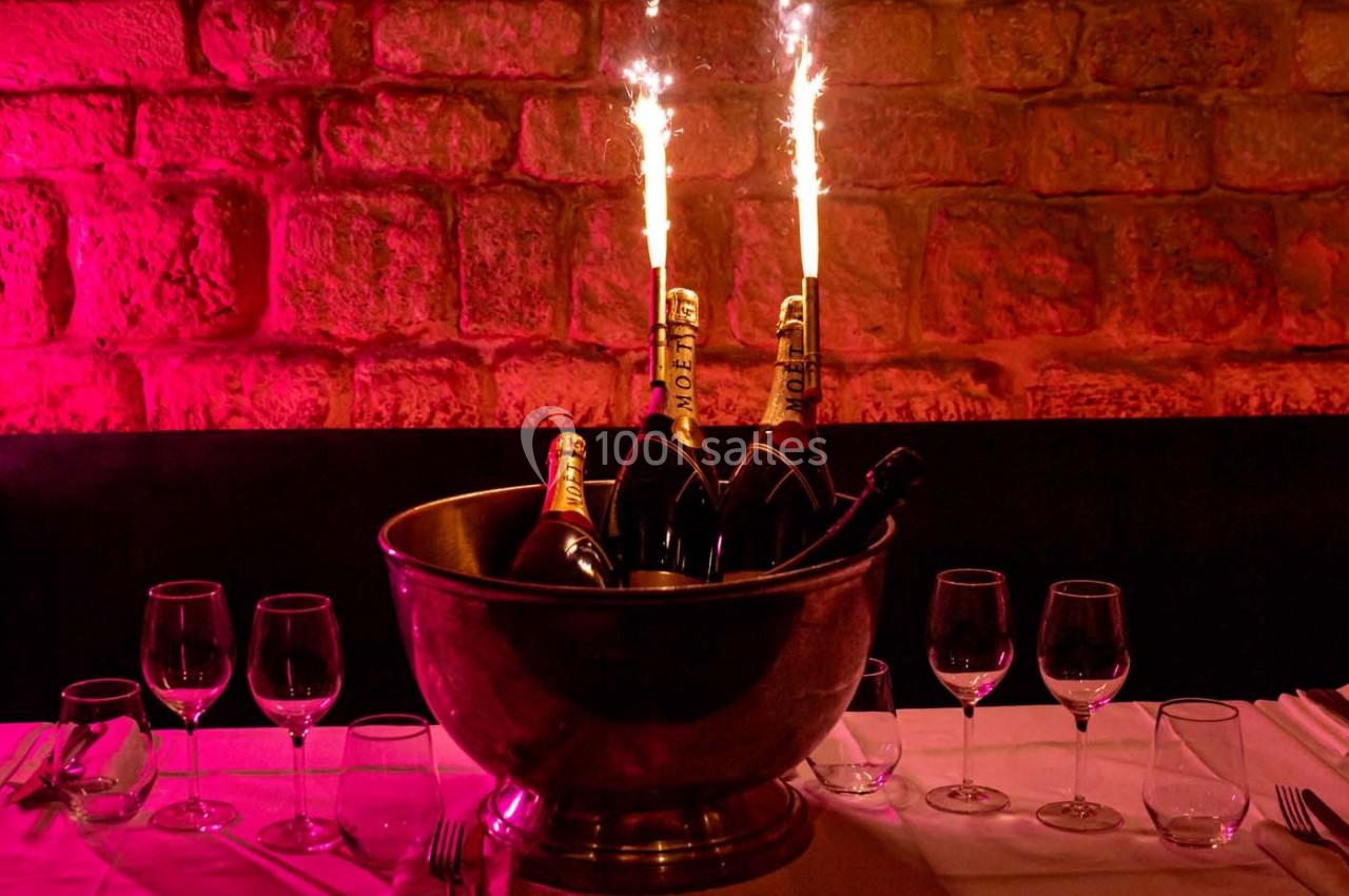 Seau rempli de bouteilles de champagne avec des cierges magiques allumés, posé sur une table dressée.