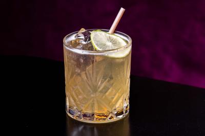 Cocktail jaune orangé garni d’un demi-fruit de la passion, accompagné d’un verre de champagne sur un comptoir en bois.