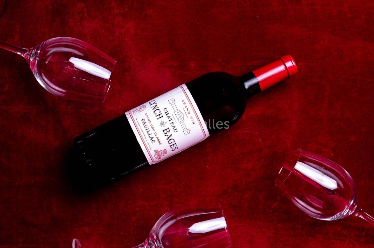 Bouteille de vin rouge posée sur une surface rouge entourée de quatre verres à vin vides.