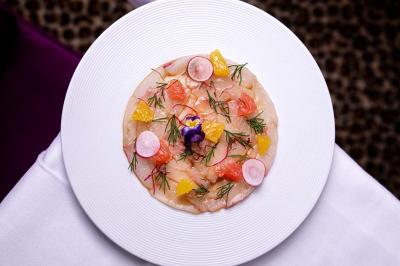 Cocktail jaune orangé garni d’un demi-fruit de la passion, accompagné d’un verre de champagne sur un comptoir en bois.