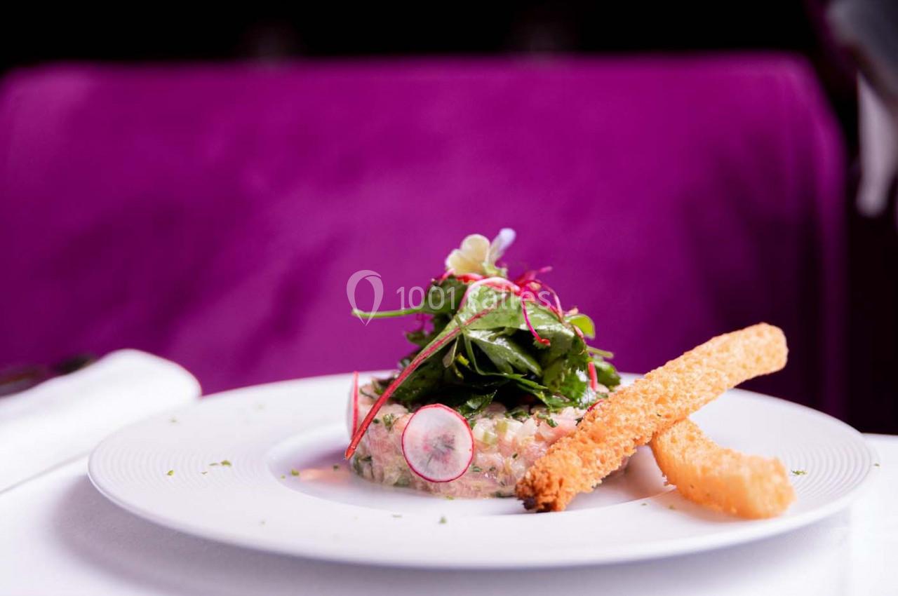 Plat raffiné composé de tartare, salade verte, radis tranchés et deux bâtonnets croustillants sur une assiette blanche.