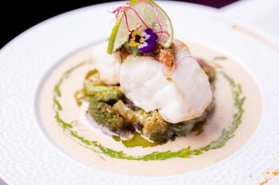 Cocktail jaune orangé garni d’un demi-fruit de la passion, accompagné d’un verre de champagne sur un comptoir en bois.