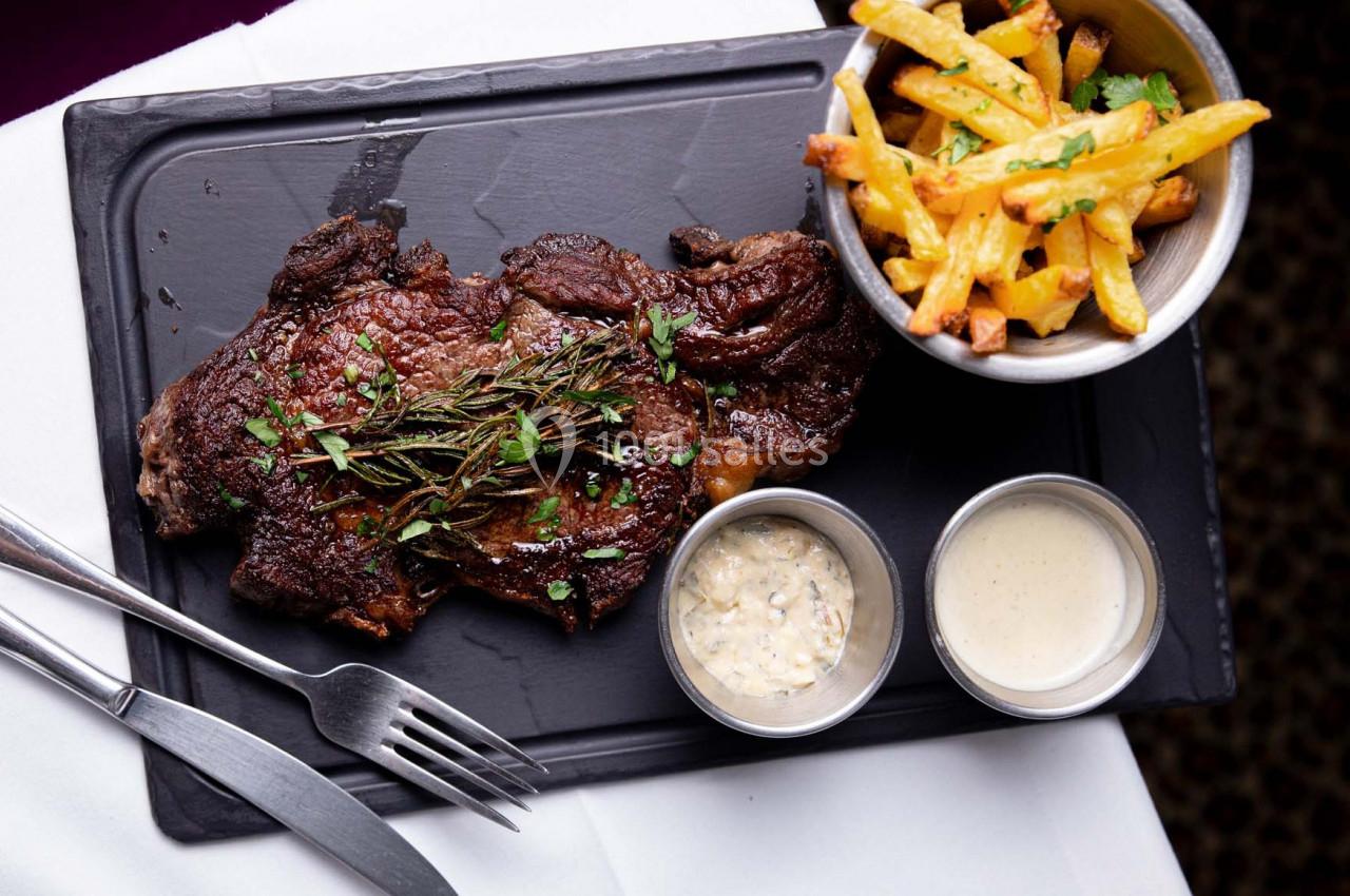 Steak grillé garni d'herbes, accompagné de frites et de deux sauces, servi sur une ardoise noire.
