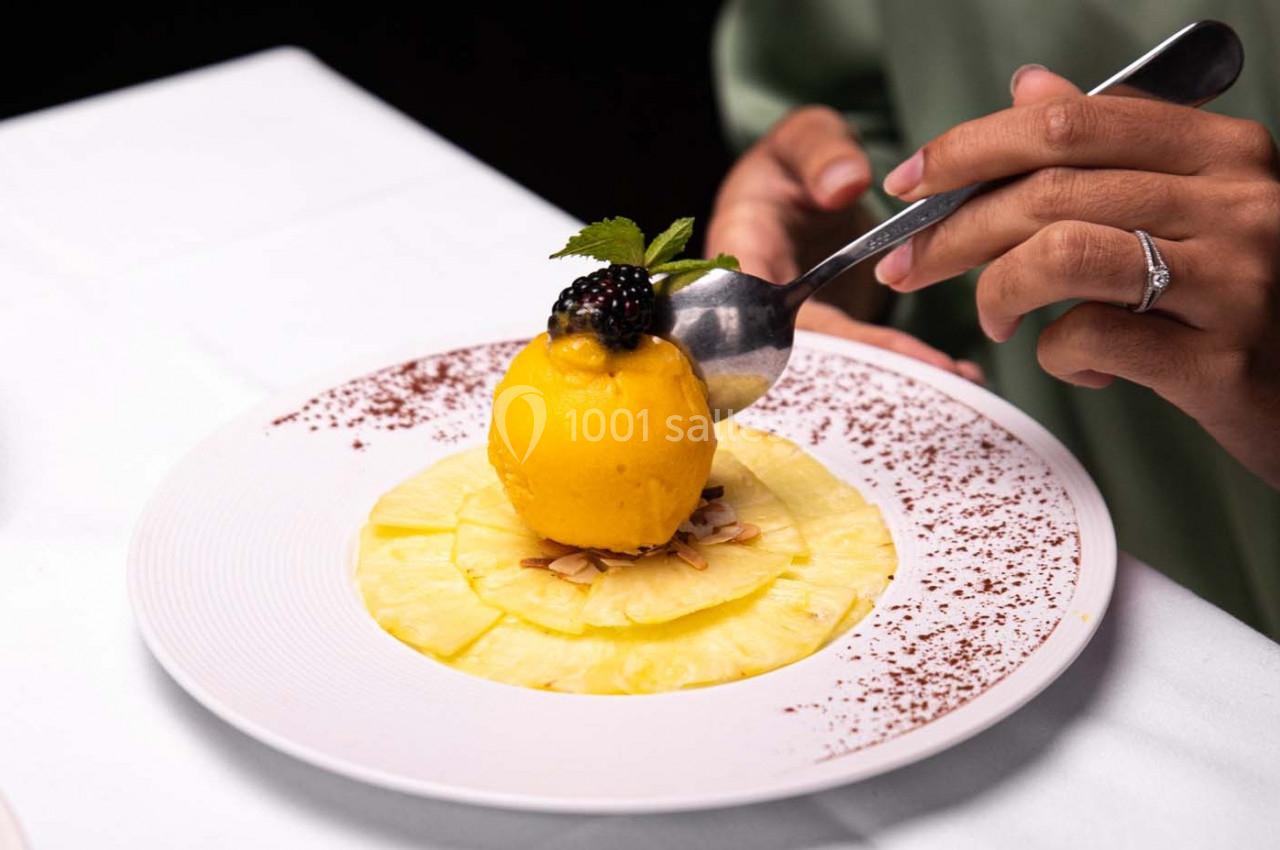 Dessert composé d'une boule de sorbet mangue sur des tranches d'ananas, décoré de fruits rouges et d'amandes effilées.