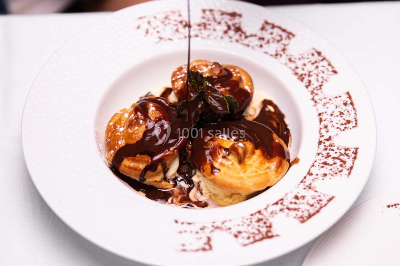 Profiteroles nappées de sauce au chocolat servies dans une assiette blanche décorée de poudre de cacao.