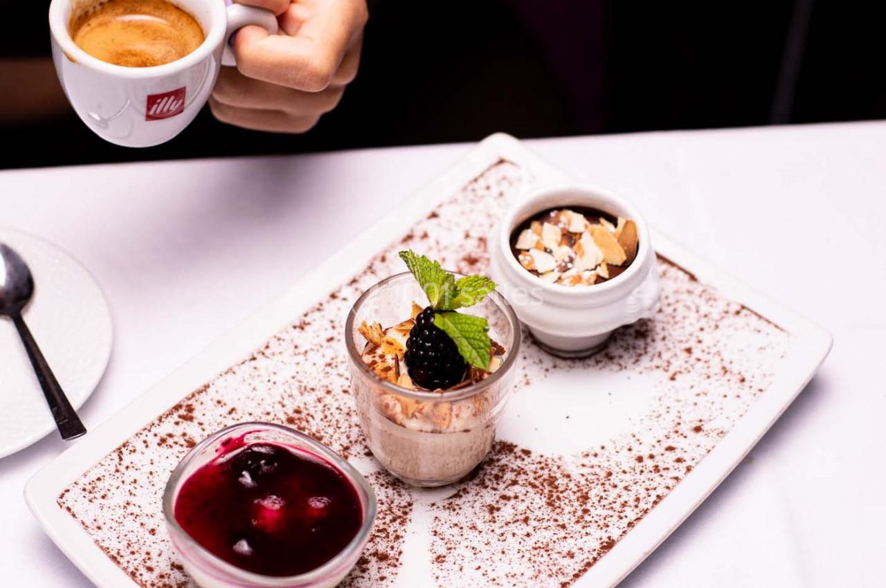Assiette de desserts variés avec mousse, coulis de fruits rouges et éclats d'amandes, accompagnée d'une tasse de café.