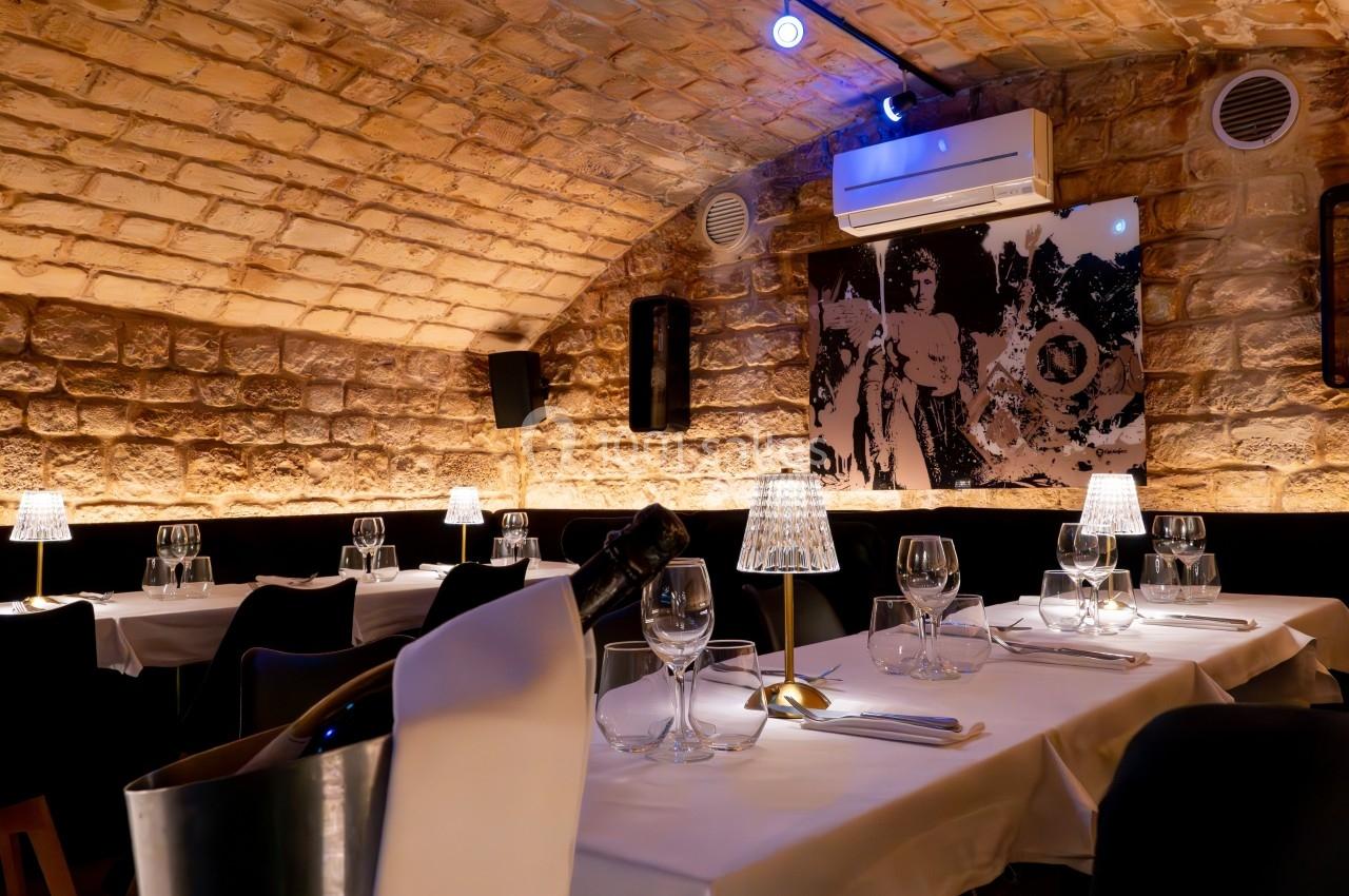 Salle de restaurant voûtée avec murs en pierre, tables dressées, éclairage tamisé et décoration murale.
