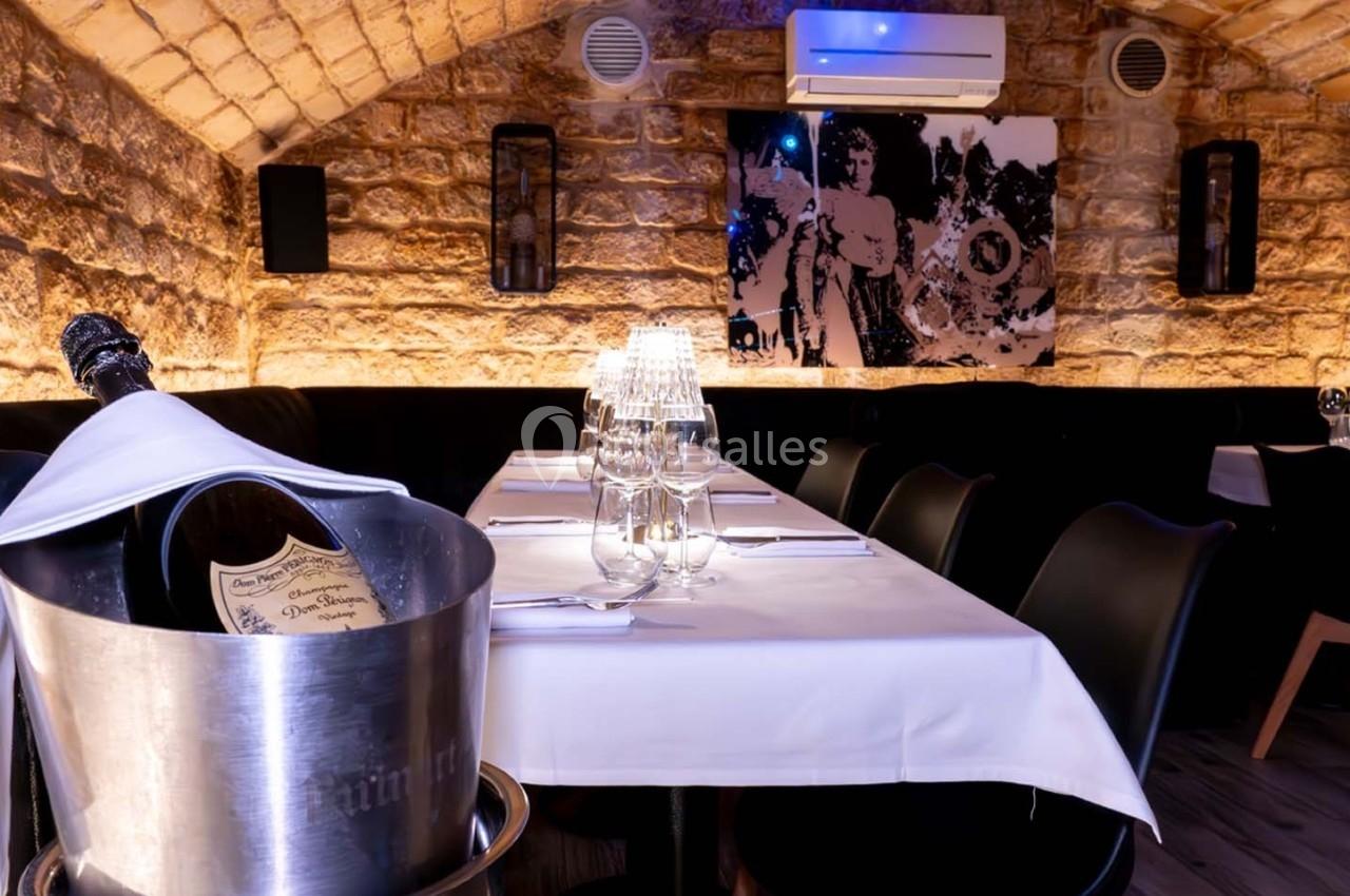 Salle de restaurant voûtée en pierre, table dressée avec nappes blanches, bouteille de champagne dans un seau.