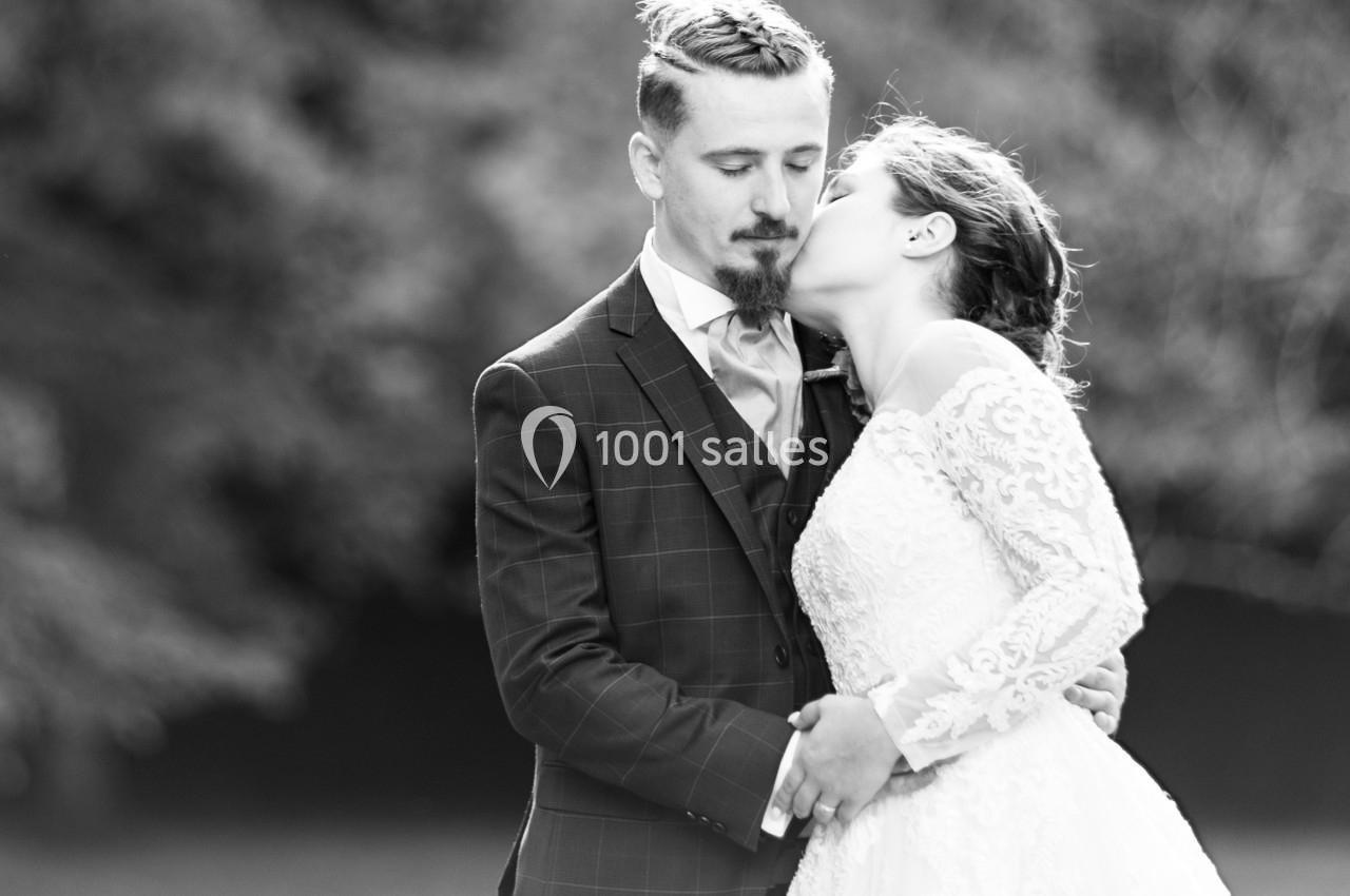 Un couple en tenue de mariage s'embrasse tendrement dans un cadre extérieur flou.