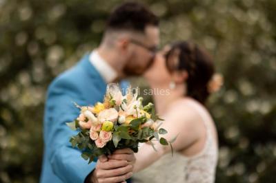 Un couple s'embrasse en arrière-plan tandis qu'un bouquet de fleurs est mis au premier plan.
