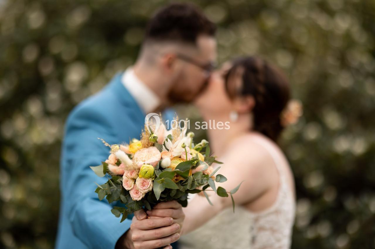 Un couple s'embrasse en arrière-plan tandis qu'un bouquet de fleurs est mis au premier plan.