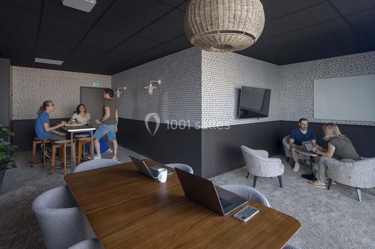 Espace de travail partagé avec tables, chaises, ordinateurs et personnes discutant dans une ambiance moderne et lumineuse.