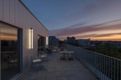 Terrasse moderne avec mobilier extérieur, vue sur une ville au coucher du soleil et ciel aux teintes orangées.