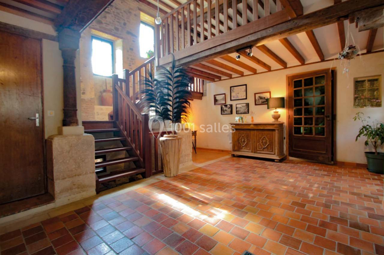 Intérieur d'une maison avec escalier en bois, sol en carreaux de terre cuite et mobilier rustique.