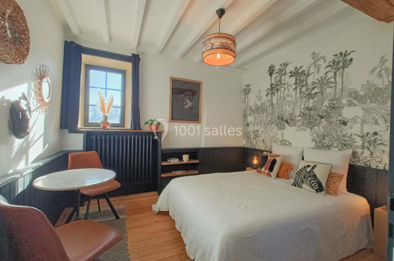 Chambre lumineuse avec lit double, table ronde, chaises en cuir et décoration murale tropicale en noir et blanc.