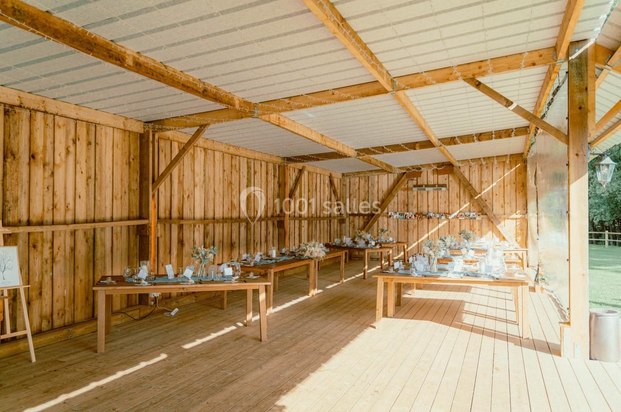 Salle en bois ouverte avec de grandes tables décorées pour un événement, éclairée par la lumière naturelle.
