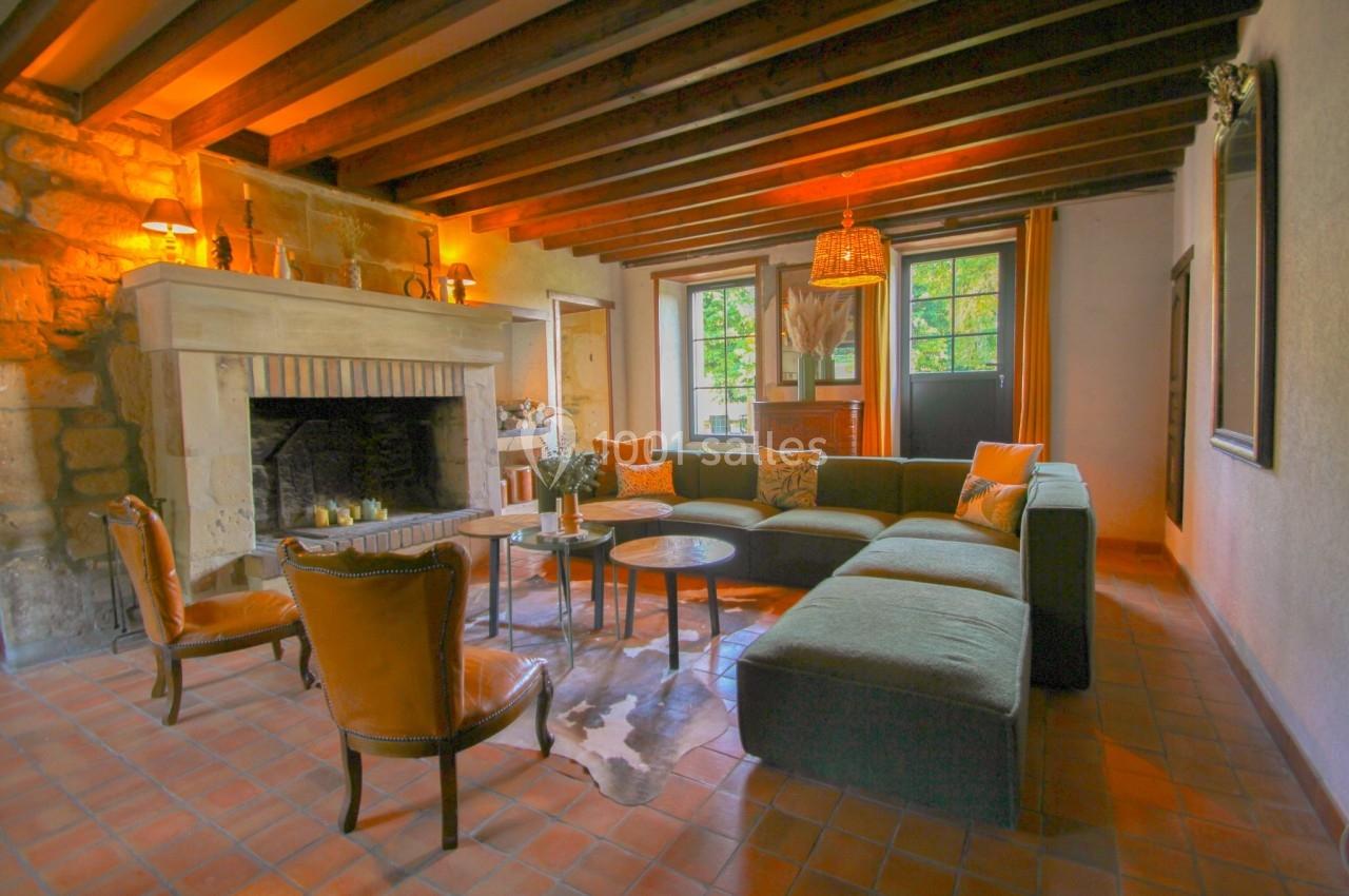 Salon chaleureux avec poutres apparentes, cheminée en pierre, canapé d'angle et fauteuils en cuir sur sol en terre cuite.