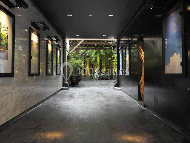 Passage couvert avec murs sombres, éclairage encastré et vue sur un espace extérieur verdoyant au fond.