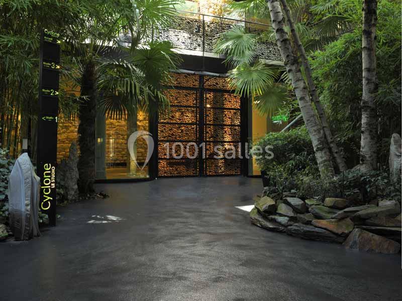 Entrée d'un espace entouré de végétation luxuriante avec un sol sombre et une signalisation lumineuse.