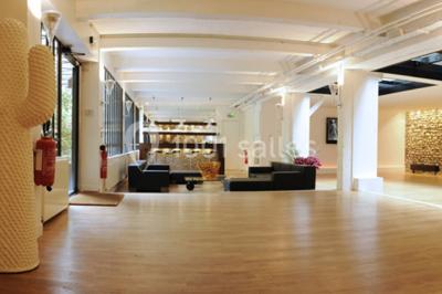 Salle lumineuse avec parquet, mobilier moderne, œuvres d'art au mur et grandes fenêtres laissant entrer la lumière naturelle.