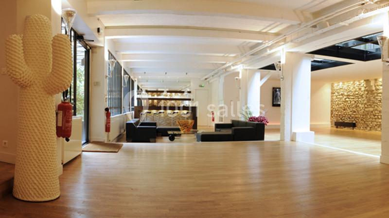 Espace intérieur lumineux avec parquet, murs blancs, canapé noir, cactus décoratif et pierres apparentes.