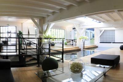 Salle lumineuse avec parquet, mobilier moderne, œuvres d'art au mur et grandes fenêtres laissant entrer la lumière naturelle.