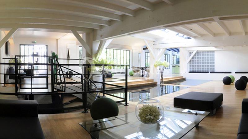 Espace intérieur lumineux avec poutres apparentes, mobilier moderne, baies vitrées et décoration végétale.