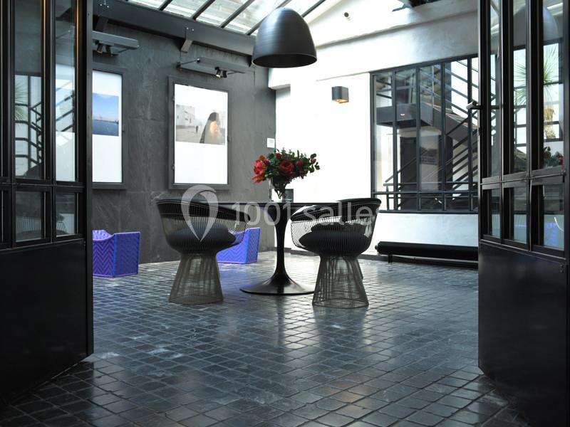 Espace intérieur moderne avec table ronde, deux chaises design et lumière naturelle entrant par une verrière.