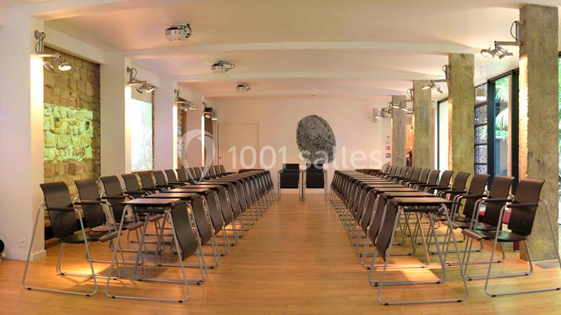 Salle de conférence lumineuse avec des rangées de chaises noires alignées et un mur décoré d'une œuvre artistique.