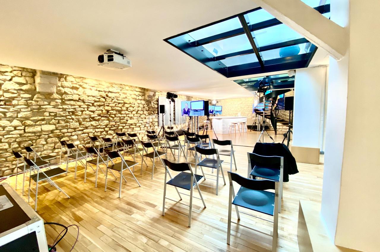 Salle de conférence lumineuse avec murs en pierre, chaises pliantes alignées et équipements audiovisuels installés.