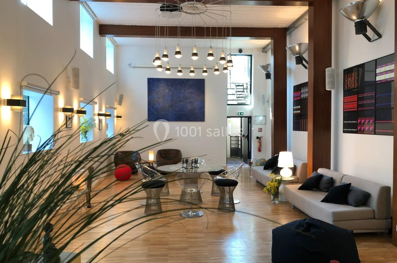 Salle lumineuse avec parquet, mobilier moderne, œuvres d'art au mur et grandes fenêtres laissant entrer la lumière naturelle.