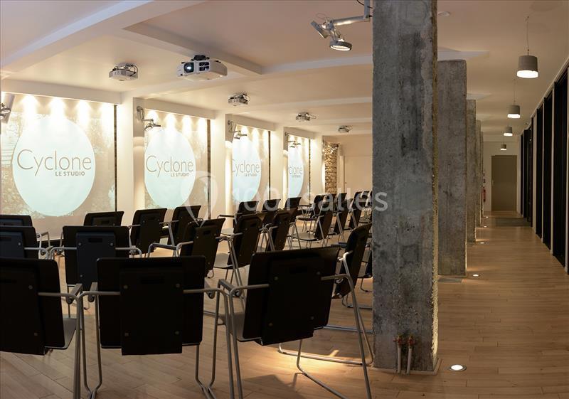 Salle de conférence moderne avec rangées de chaises noires, projecteurs au plafond et murs éclairés.