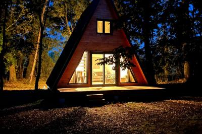 Cabane en forme de A éclairée de l'intérieur, entourée d'arbres dans un environnement nocturne.